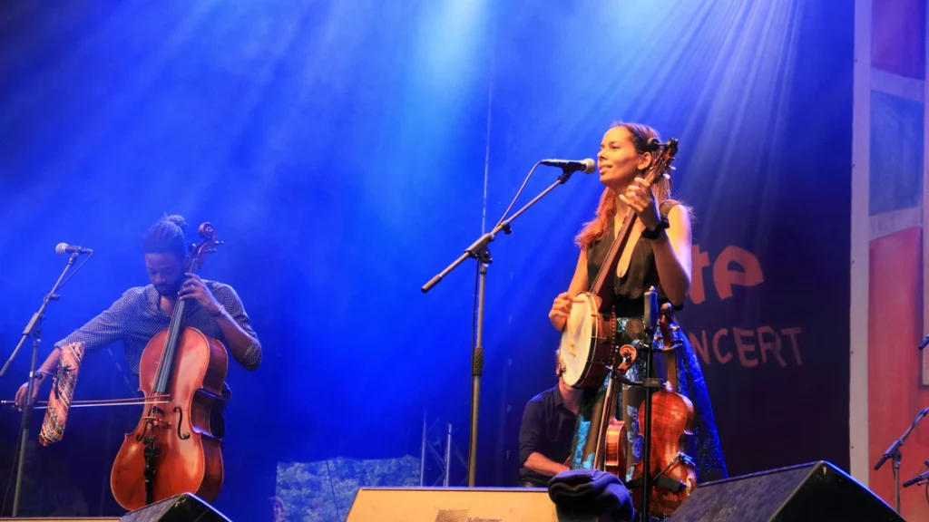 Rhiannon Giddens playing banjo at the microphone with a cellist beside her under blue light